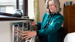 Cold to Cosy Home Energy-saving. Elderly Woman fitting reflector behind radiator